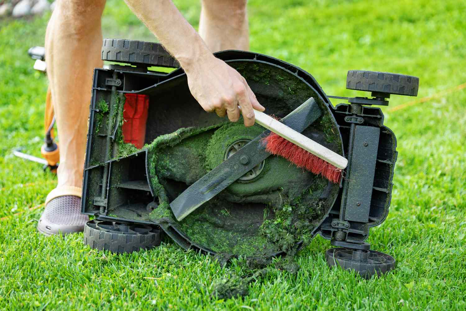 Personne nettoyant le dessous du plateau de la tondeuse avec une brosse.