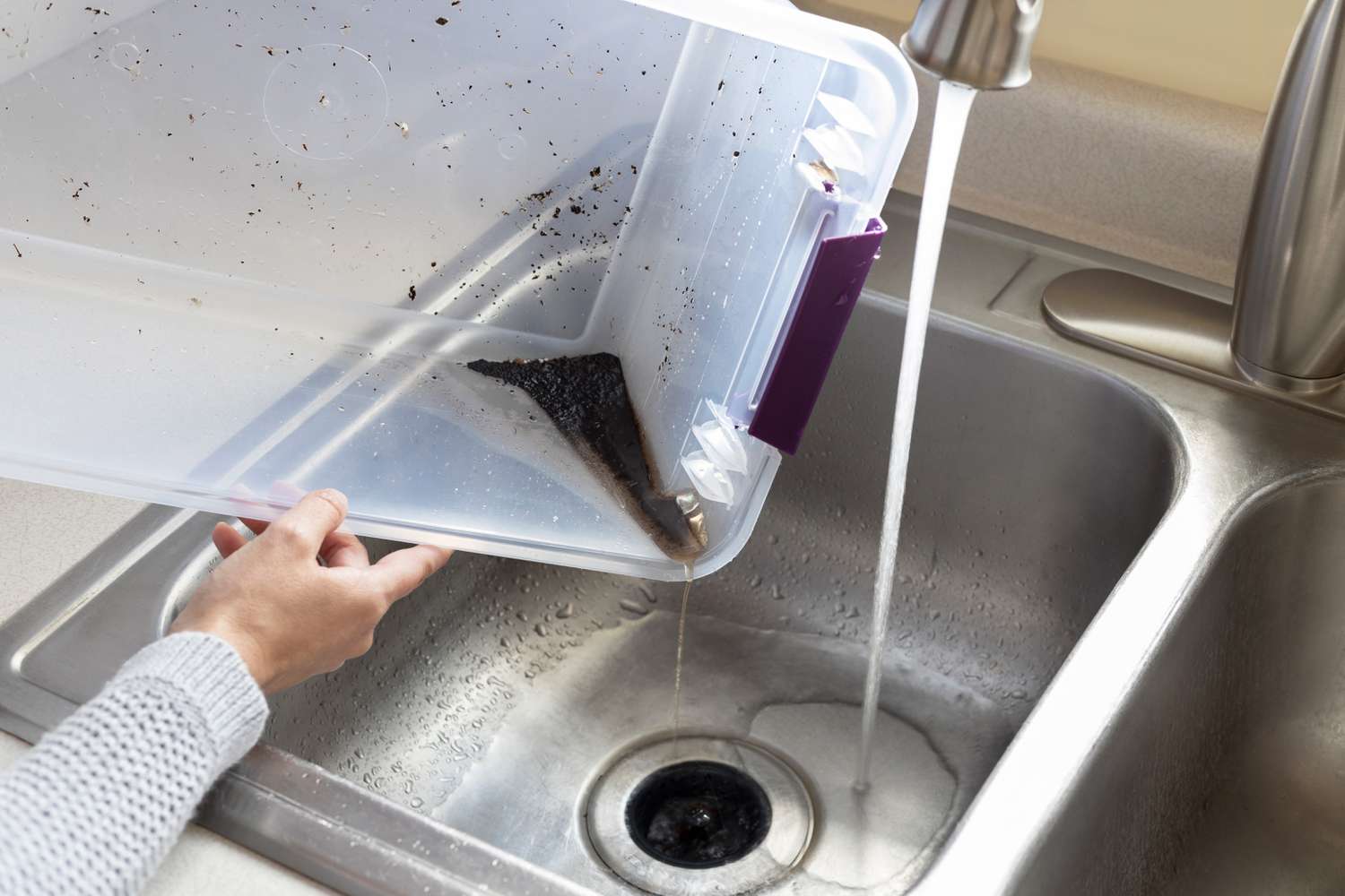 Bac à compost vidé et nettoyé dans l'évier de la cuisine avec de l'eau courante.