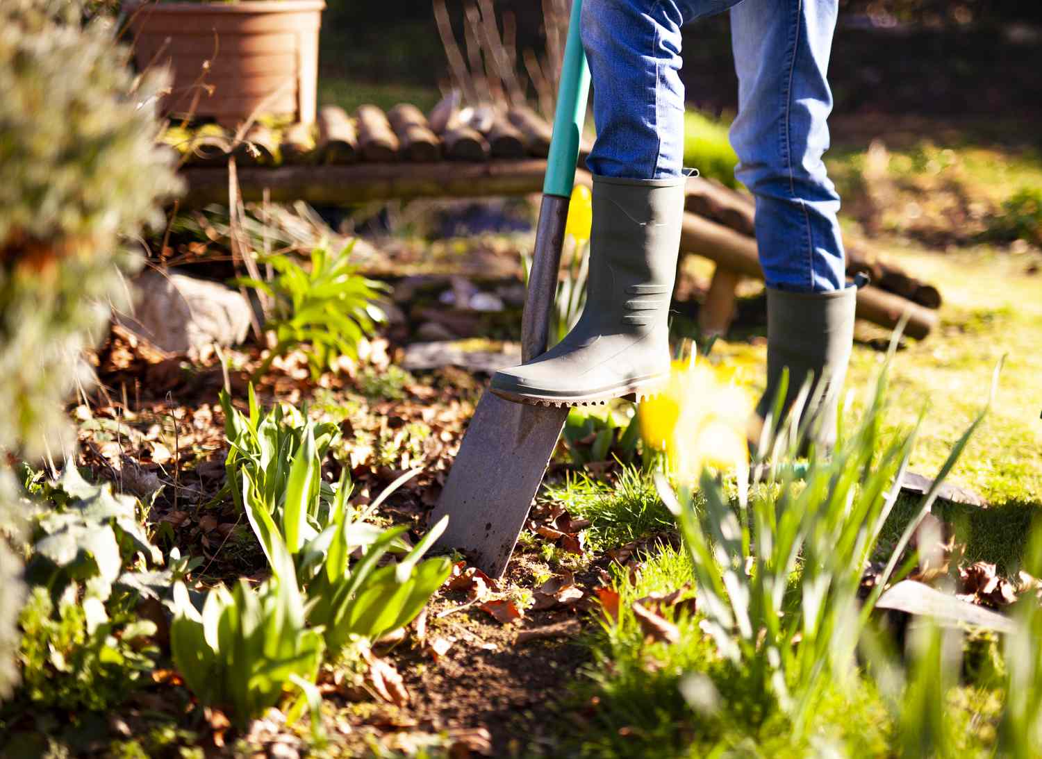 Jardinier en bottes de caoutchouc creusant un trou étroit à l'aide d'une bêche à lapin.