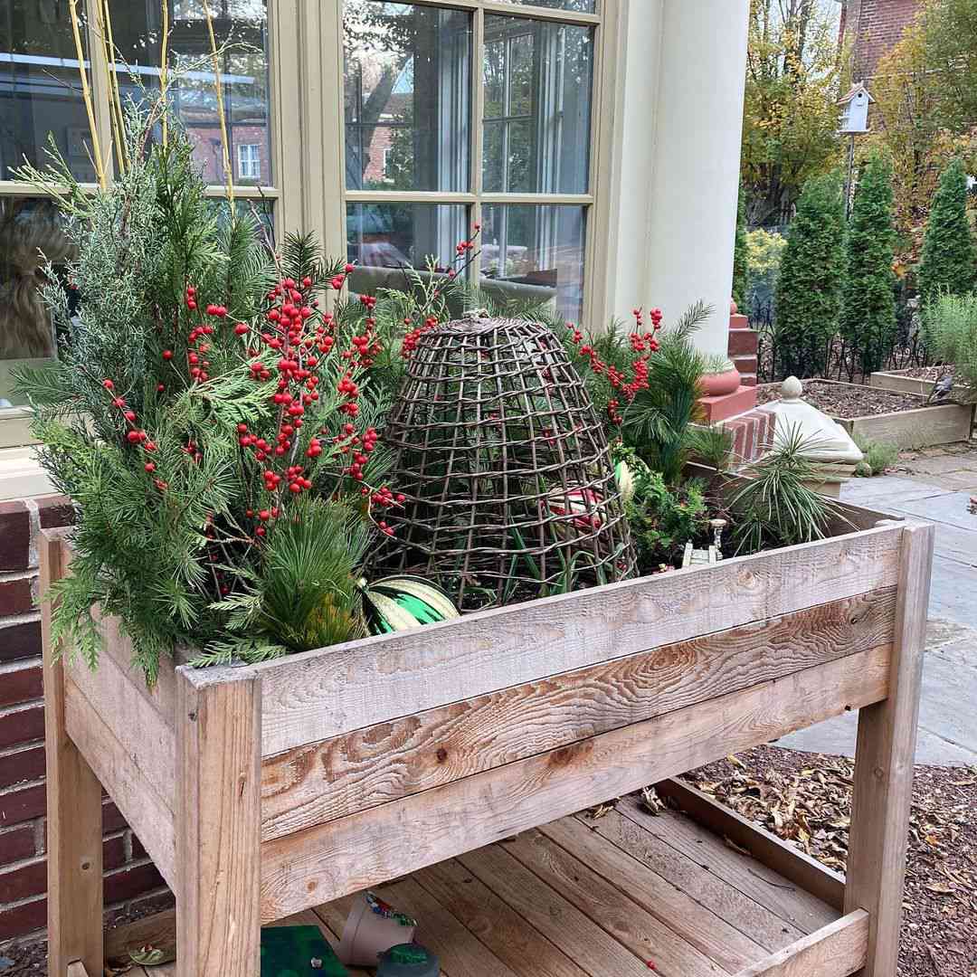 Jardinière en bois sur pied avec verdure naturelle, baies rouges et cloche en osier