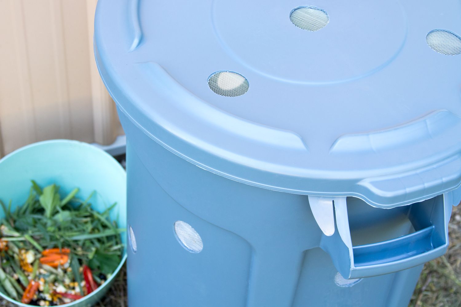 Composteur bleu clair en forme de poubelle à côté d'un seau de déchets alimentaires.