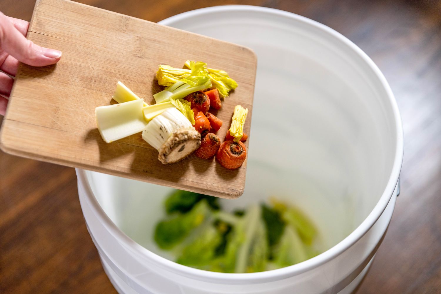 Seau Bokashi dans lequel sont versés des déchets alimentaires provenant d'une planche à découper.