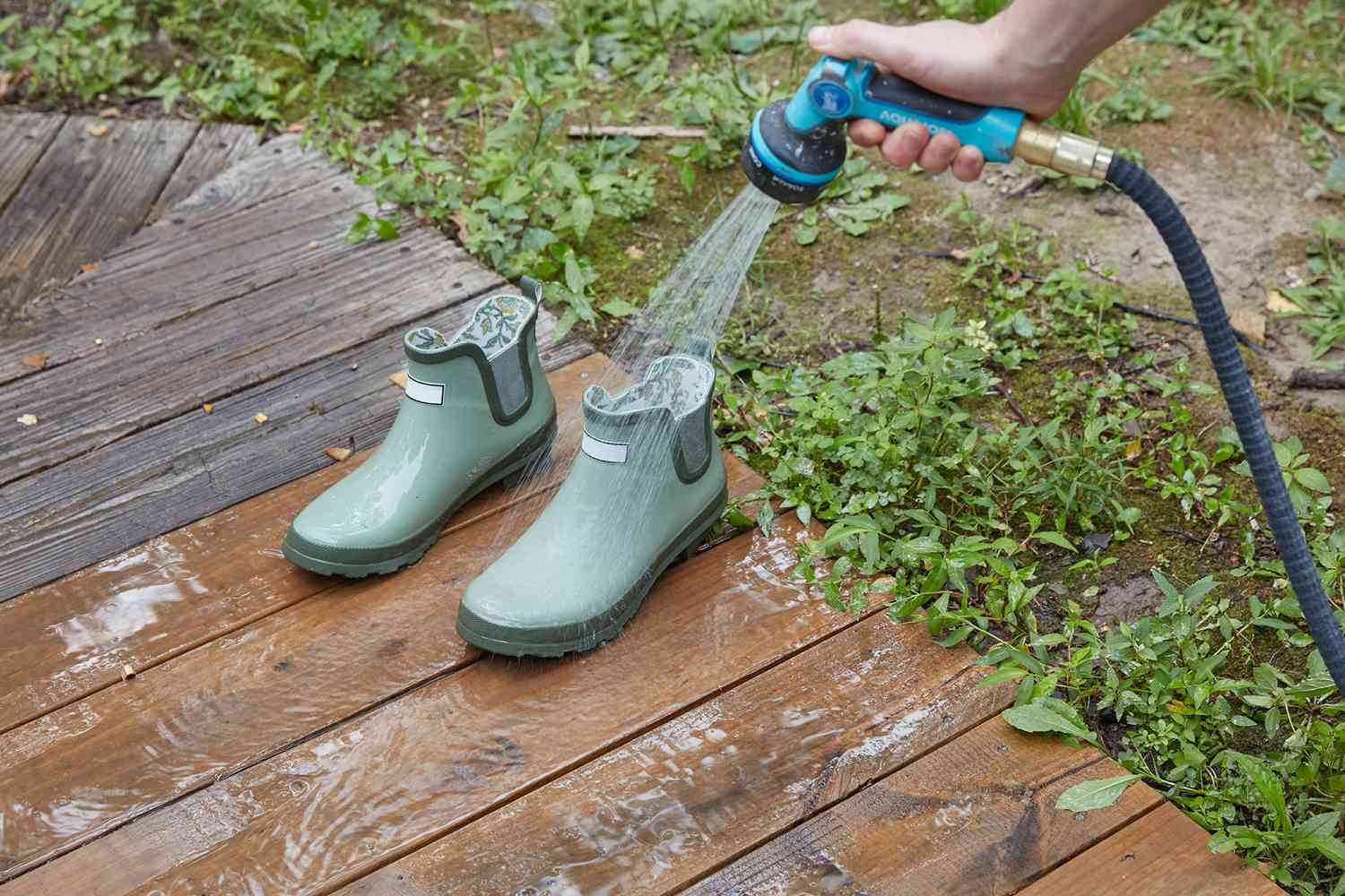 Bottes de jardin en caoutchouc nettoyées à l'eau savonneuse à l'aide d'un tuyau d'arrosage.